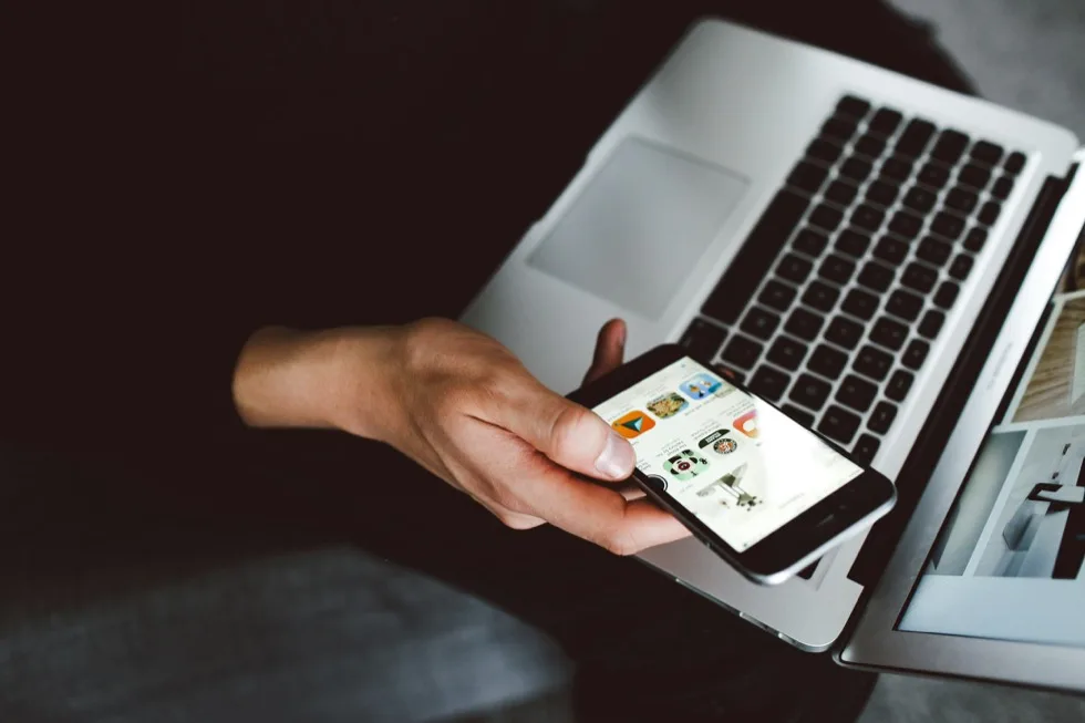 A hand holding a phone over an open laptop.